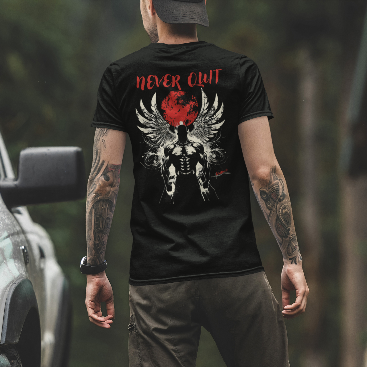 resilient man next to his car wearing a black t-shirt featuring a muscular winged figure with a red moon background and the phrase 'Never Quit' in bold red text, complemented by the DubBeast logo